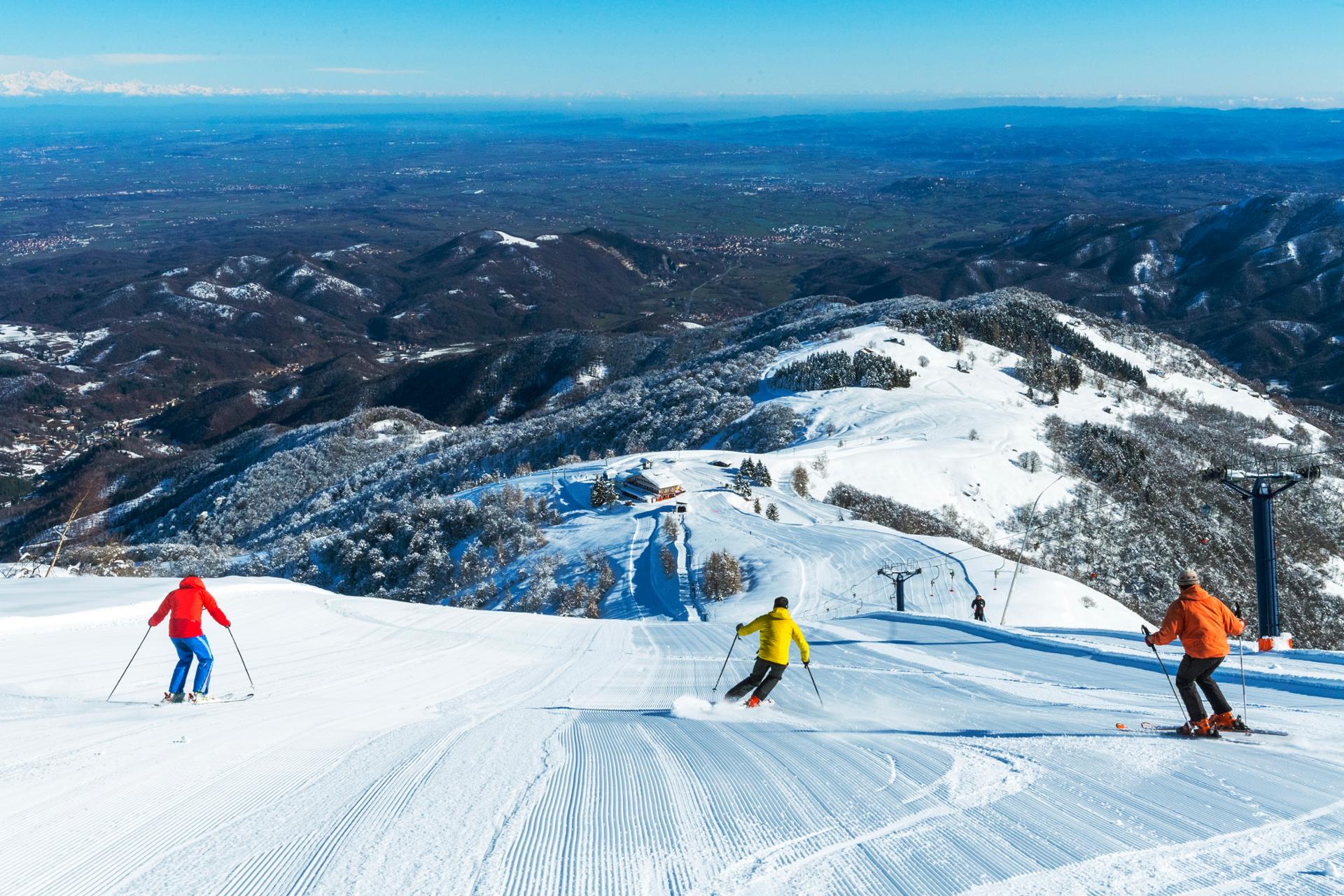 Winter sports scene at Lurisia Monte Pigna, Piedmont, Italy, featuring a skier gliding down a scenic ski resort, with a ski lift in the background.