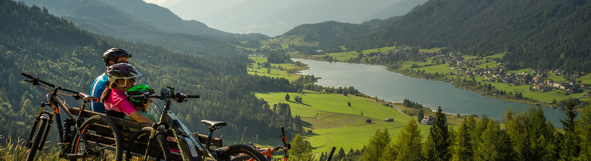 A mountain biker is enjoying a sunny day in Naggler Alm Naturpark Weissensee Austria amid a backdrop of a quaint chalet and majestic mountains creating a serene winter sports scene.