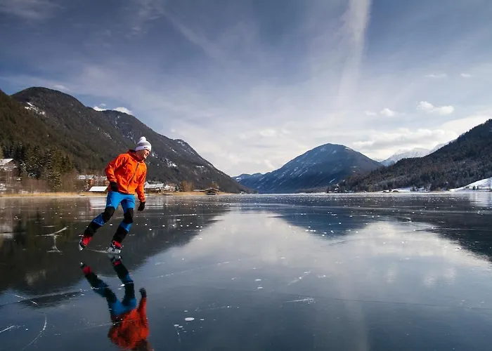 Winter scene at Naggler Alm in Naturpark Weissensee, Austria showcasing a skier descending snowy slopes amid a picturesque winter landscape with a winter sports center in the background.