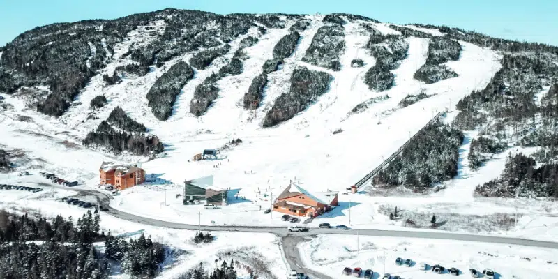 View of White Hills Ski Resort in Clarenville, Newfoundland and Labrador featuring a chalet amidst a scenic winter landscape bustling with winter sports activities.