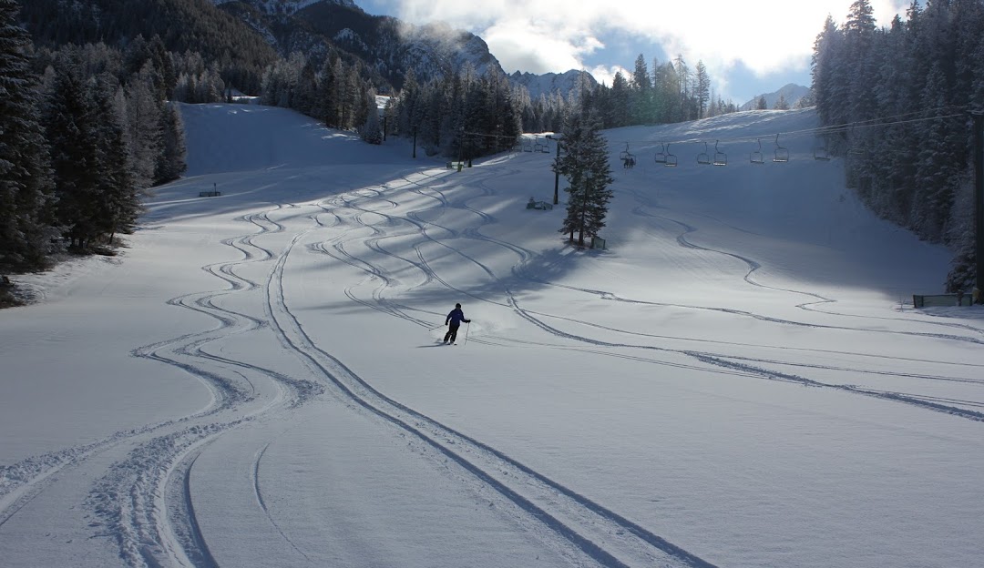 A skier glides down the slopes at Fairmont Hot Springs, surrounded by the beauty of the Kootenay Rockies. The image also features a charming chalet and a bustling winter sports centre.