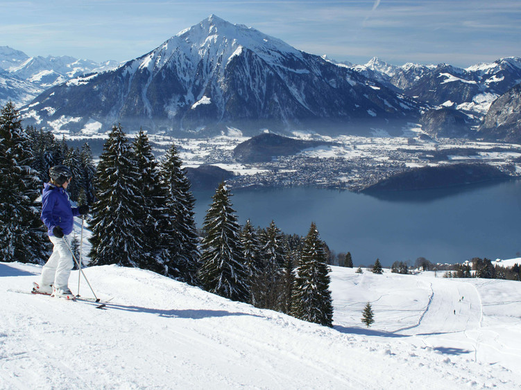 A skier enjoying a winter sports scene at the scenic Schwanden-Sigriswil in Bern, with a view of a charming chalet and ski resort in the backdrop on the shores of Lake Thun, Switzerland.