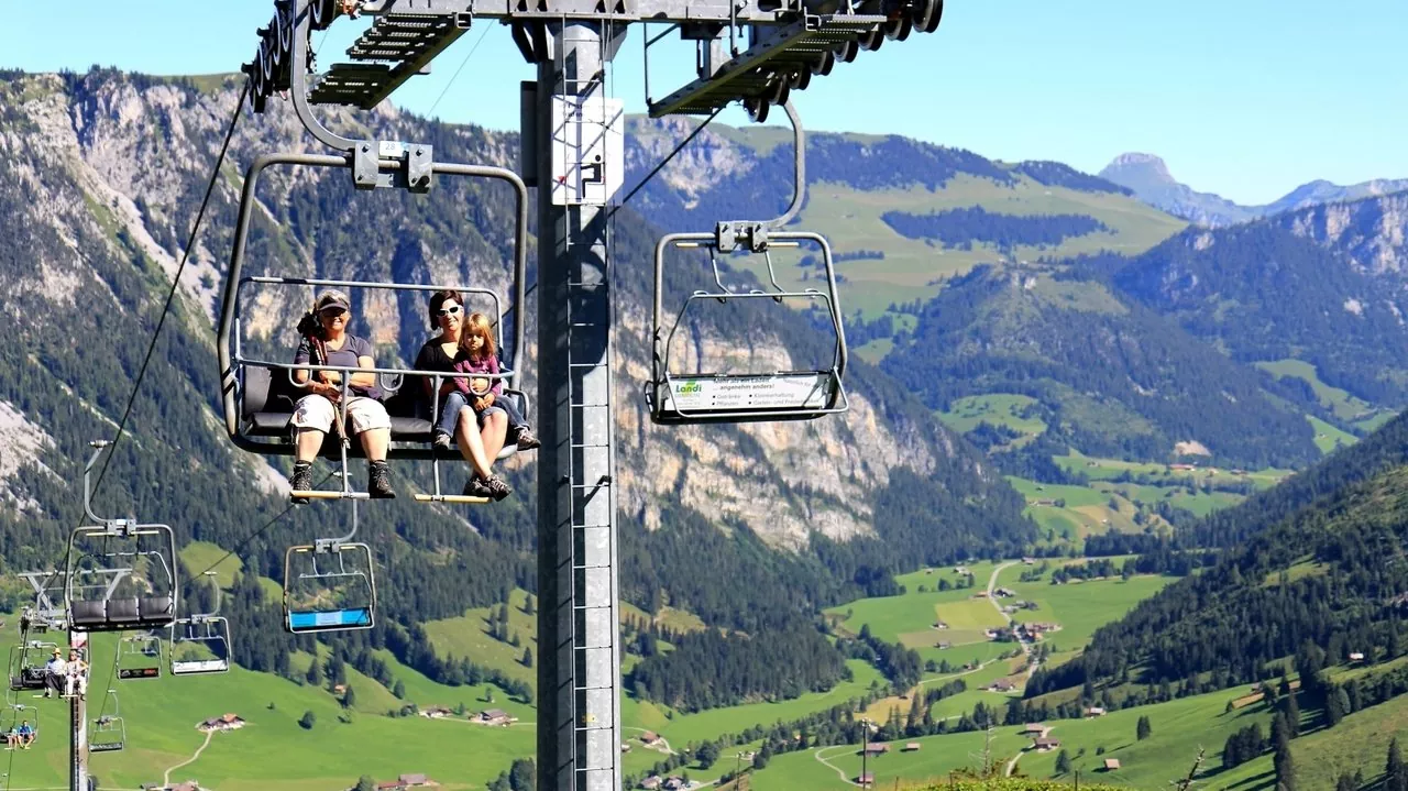 A vibrant ski resort image from Grimmialp in Switzerland's Bernese Oberland. The scene showcases a ski lift with towering peaks in the background a cozy chalet and a family enjoying winter sports.