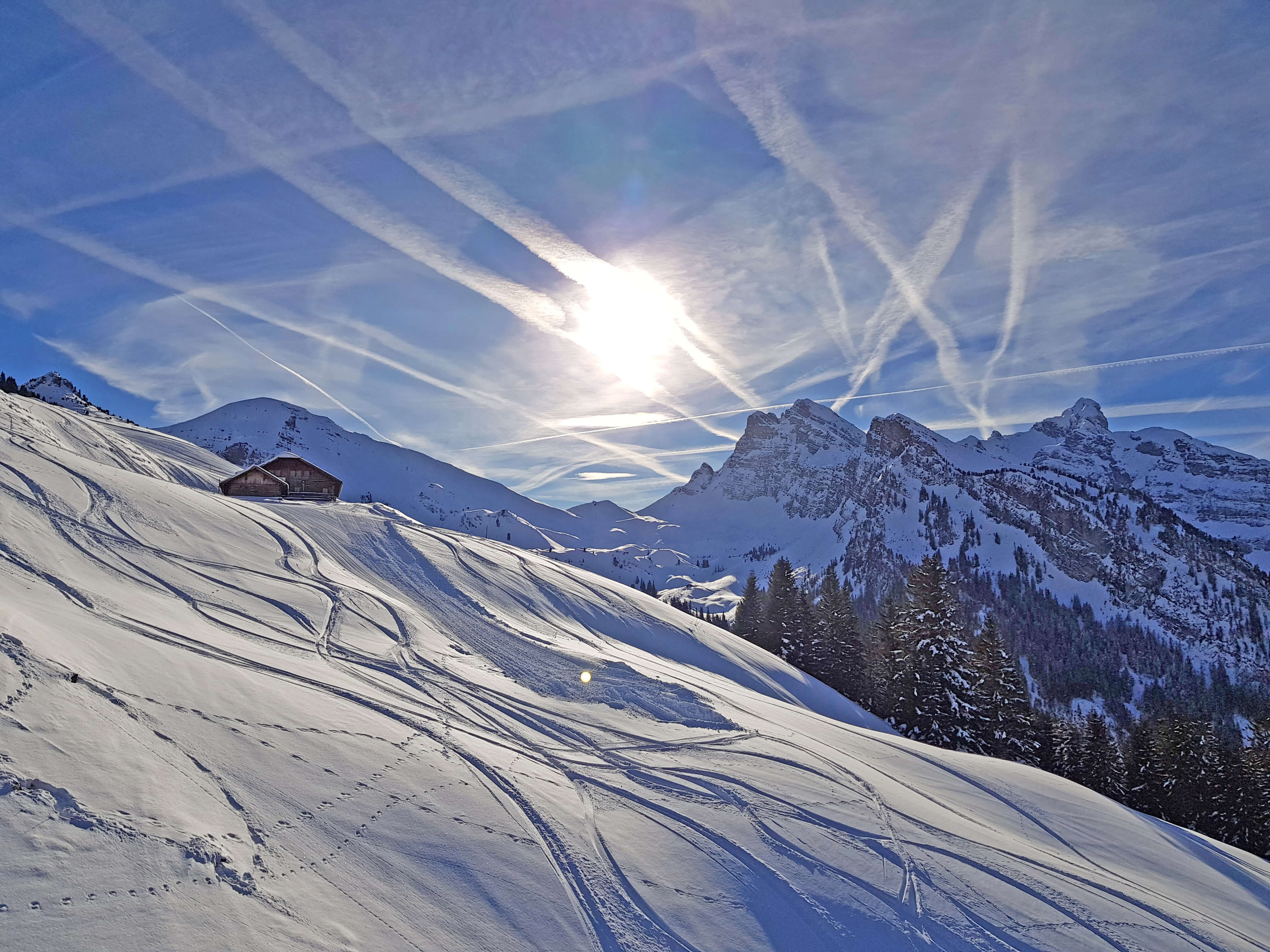 Winter sports enthusiasts enjoying a sunny day at the Grimmialp ski resort in Bernese Oberland, Switzerland, with a charming chalet and beautiful snowy landscape in the backdrop.