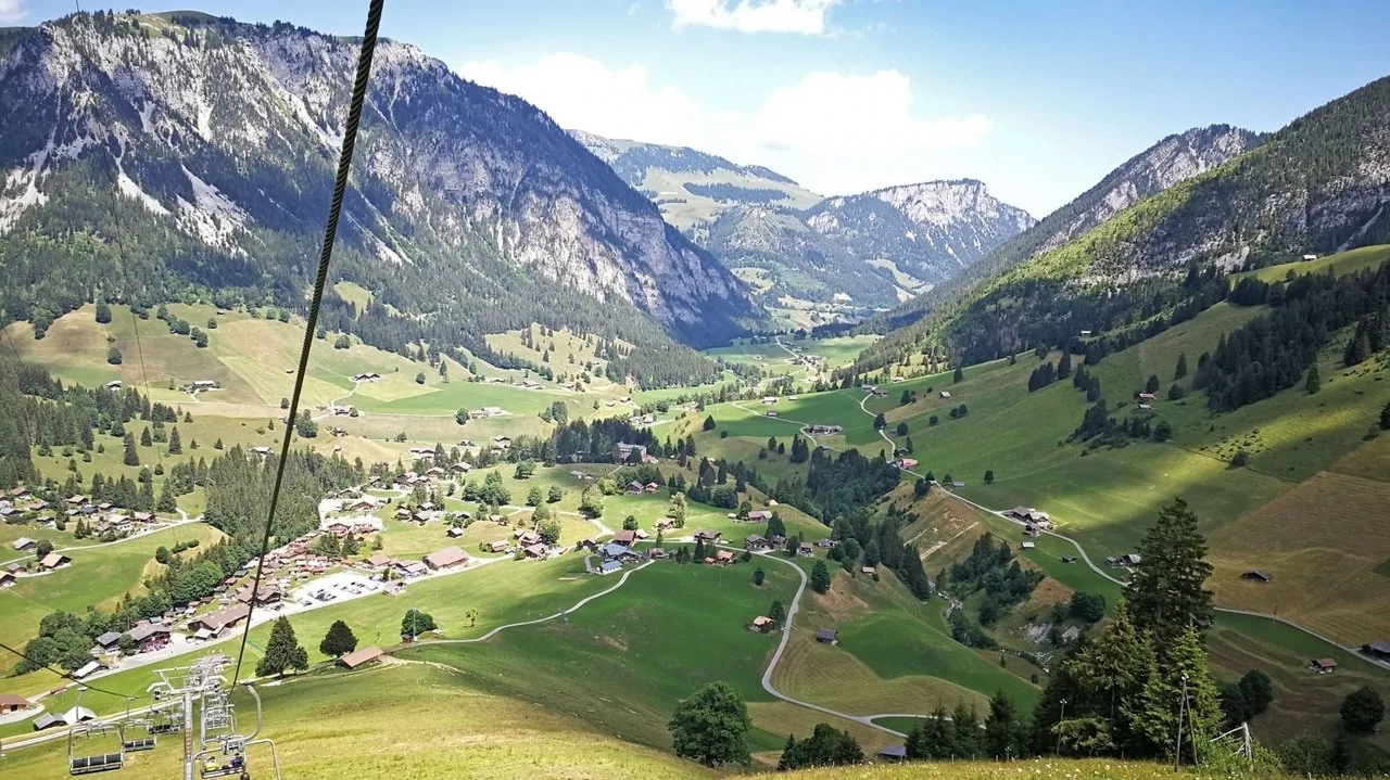 A charming chalet sits nestled at the base of a mountain in Grimmialp Switzerland part of a ski resort. A ski lift is visible in the bright sunlight of this beautiful alpine day.