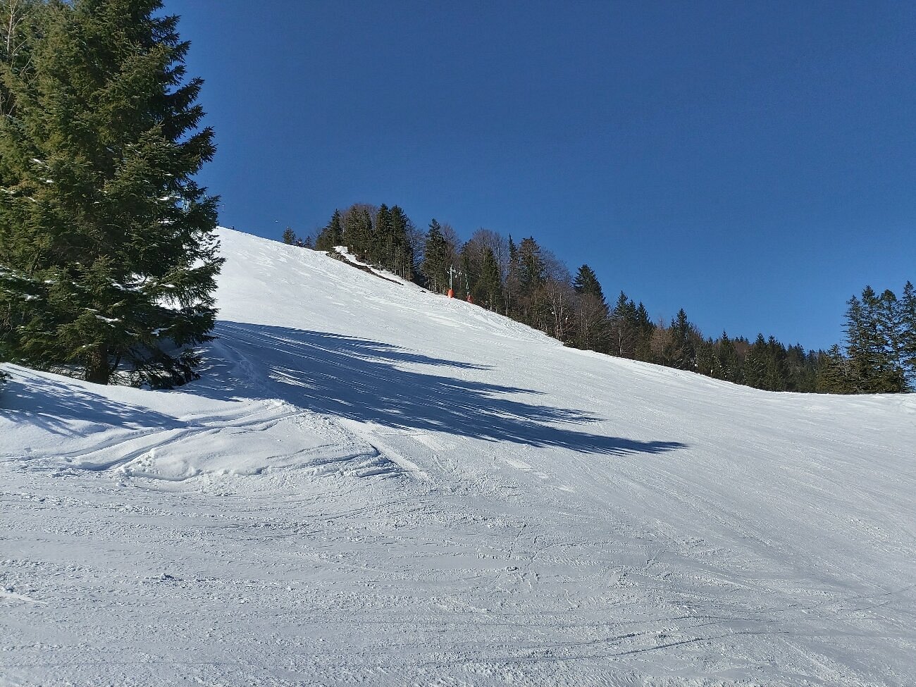A skier tears down the slopes of Kranzberg ski resort in Upper Bavaria Germany. A charming chalet nestles amid a stunning winter sports scene framed by a snow-covered mountain in the background.
