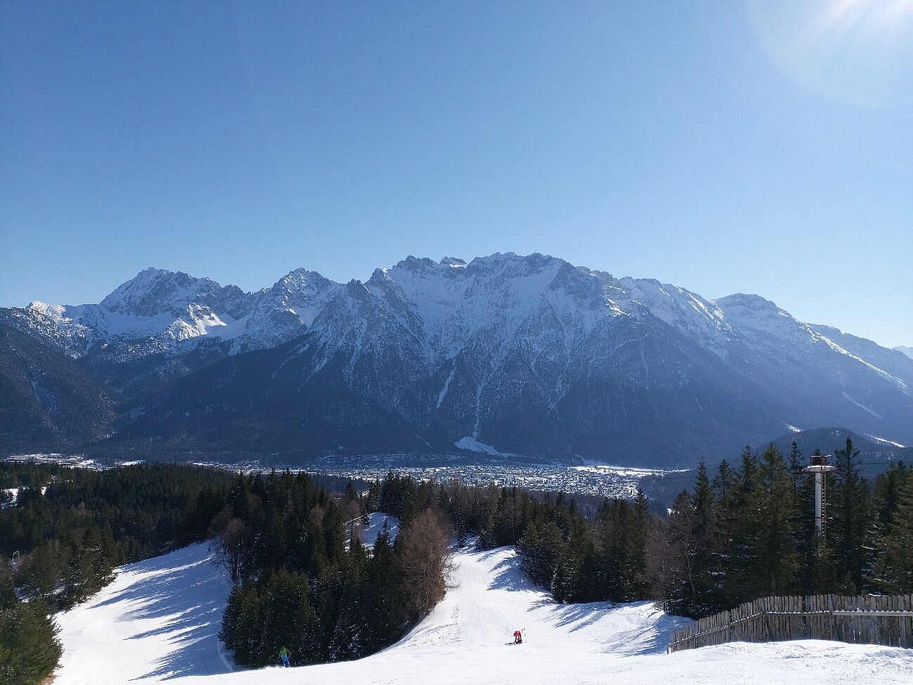 A chalet in Kranzberg Upper Bavaria stands amidst a bustling winter sports scene. You can see skiers enjoying the ski resort and the majestic mountain backdrop.