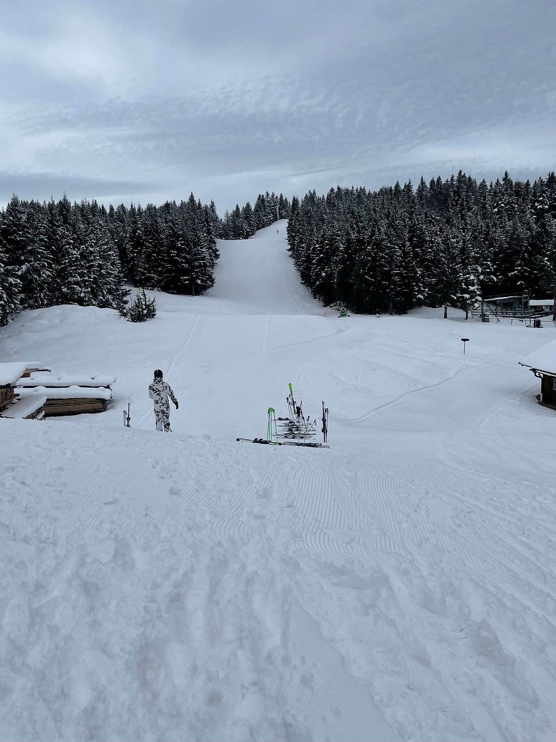 Winter sports scene at Kranzberg in Upper Bavaria, with a busy winter sports centre and ski resort. There's a quaint chalet nearby, and you can see a skier enjoying the slopes.