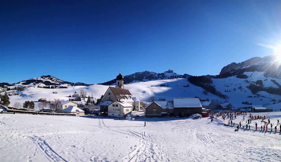 View of Ebenalp-Horn ski resort in Appenzellerland Switzerland featuring a charming chalet nestled amidst snowy winter scenery bustling with winter sports activities.