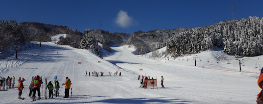 Winter sports enthusiasts enjoy a day at the Imajo 365 Ski Resort in Chūbu Minamiechizen Honshu Japan. Skiers and snowboarders descend the snowy slopes with a welcoming chalet and ski lift in the background.