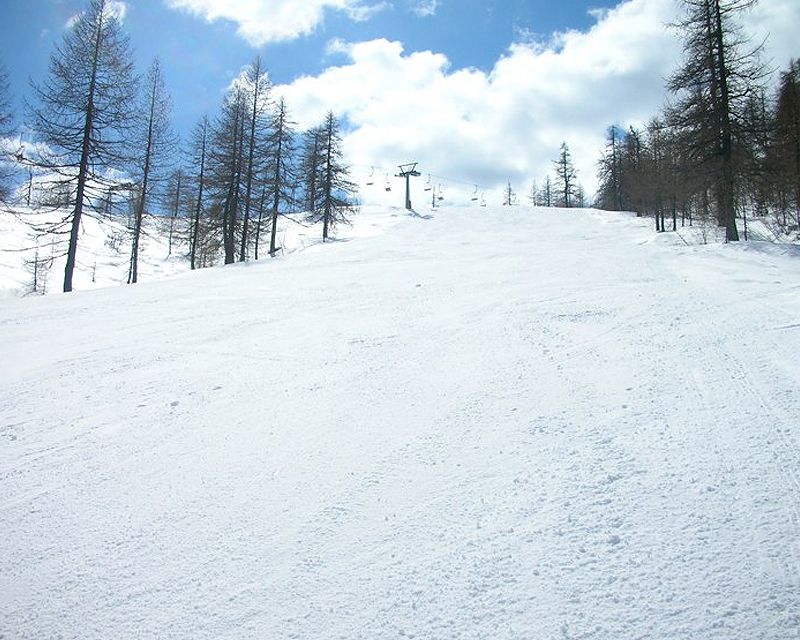 A skier navigating snow-covered slopes at Alpe Devero Ski Resort in Piedmont, Italy. A ski lift and charming challet are also visible in the winter landscape.