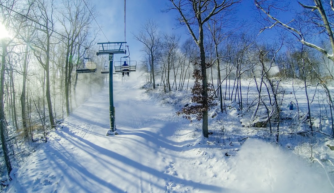Winter scene at Roundtop in Lewisberry, Pennsylvania, featuring a ski lift ascending the snowy slopes, bustling with winter sports enthusiasts at the ski resort.