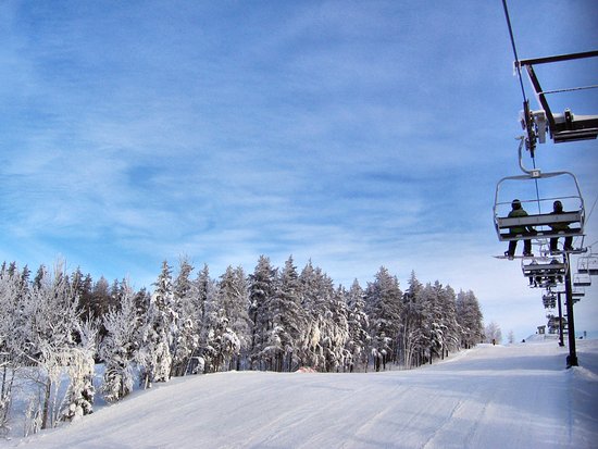 A scenic winter view at Mount Jamieson ski resort in Northern Ontario featuring a ski lift and a skier in action. A chalet can be seen in the background.