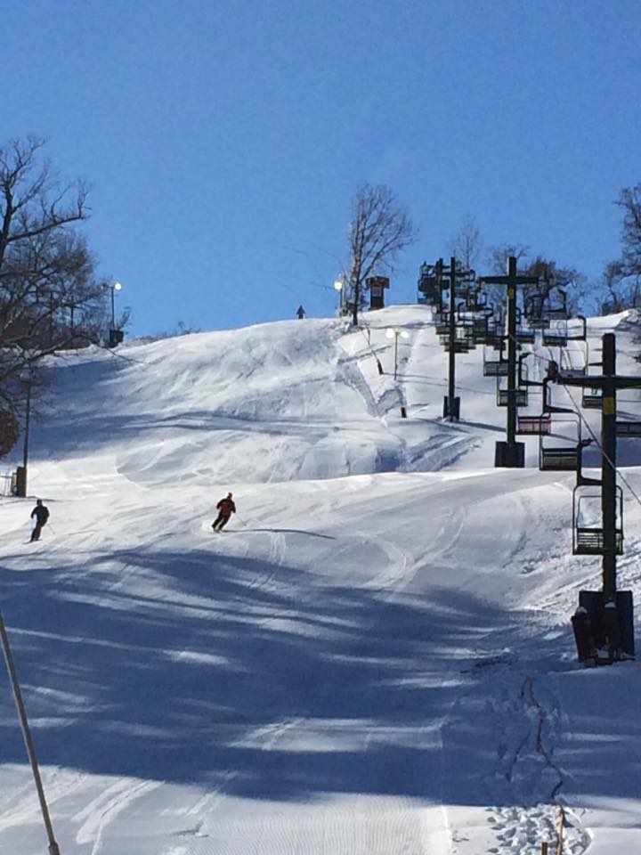 A skier effortlessly zips down a snowy slope at Mt. La Crosse ski resort in Wisconsin USA. In the background a picturesque chalet sits nestled by the mountain base and a ski lift can be seen slightly further away.