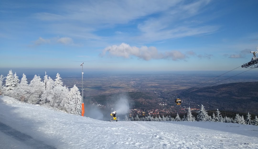 Winter sports scene at Świeradów Zdrój SKI & SUN resort in Poland featuring a skier and a ski lift near a chalet.