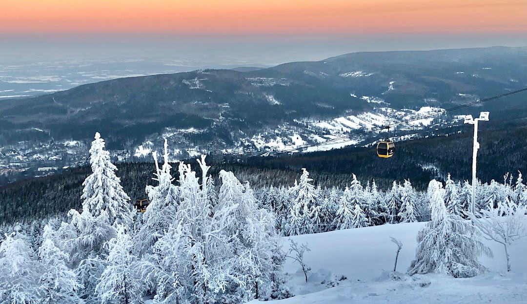 Skiers enjoying a day on the slopes at Świeradów Zdrój SKI & SUN in Poland with a ski lift visible in the background amidst stunning winter scenery.