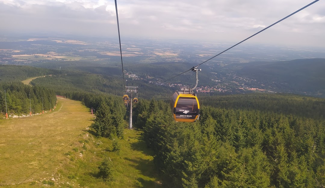 Ski lift rising above a quaint chalet at the Świeradów Zdrój SKI & SUN resort in Poland, with distant mountain landscape.