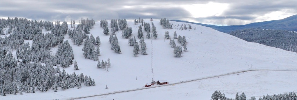 Winter scene at Sitzmark in Tonasket, Washington, showing a bustling ski resort with a ski lift operating against a backdrop of snow-covered mountains and trees.