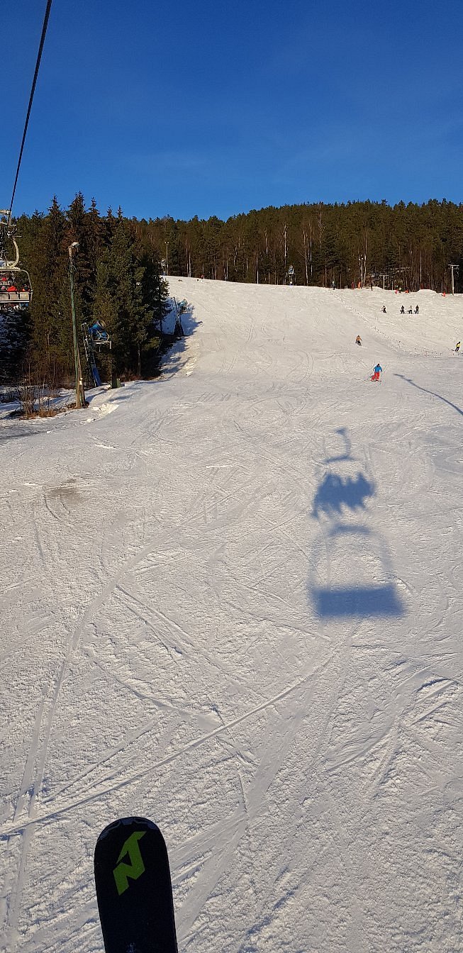 A skier enjoys a winter sports scene in Drammen Norway. A ski lift part of the ski resort stands in the background. A snowmobile can also be glimpsed nearby.