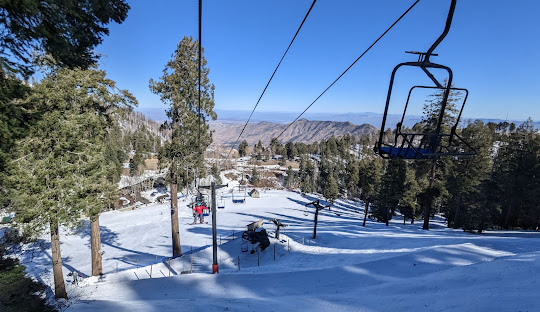 Winter scene at Mt Lemmon Ski Valley, Arizona, with a ski lift operating amidst snow-covered slopes. Skiers can be seen enjoying the resort's facilities.