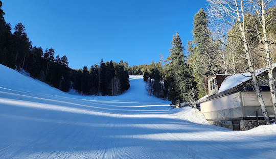 Winter scene at Mt Lemmon Ski Valley, Arizona showcasing a bustling ski resort with ski lift ferrying skiers uphill, a skier gliding downhill and chalet nestled amongst the snow-covered trees.