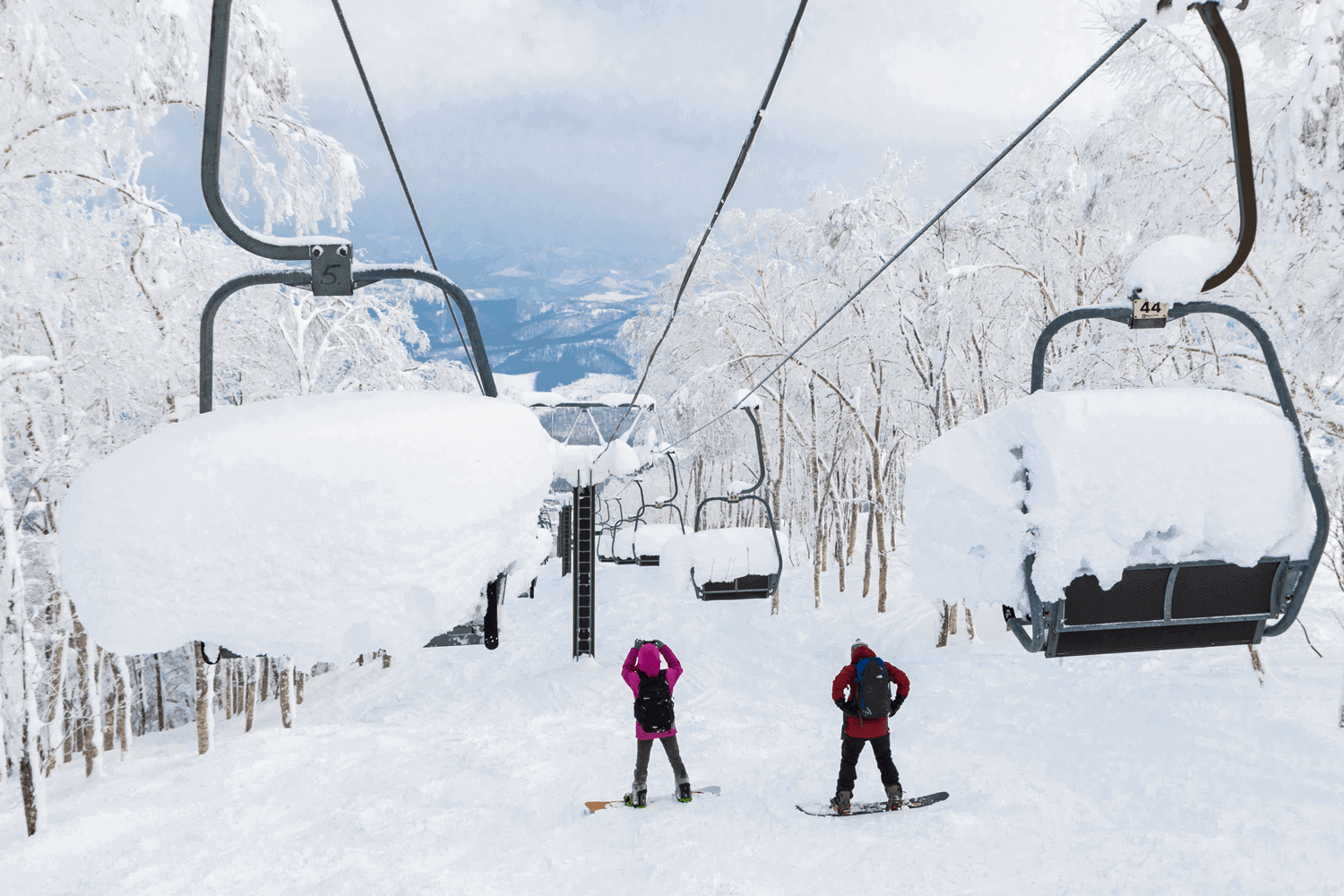 Rusutsu in Japan - two people riding a ski lift in the snow.
