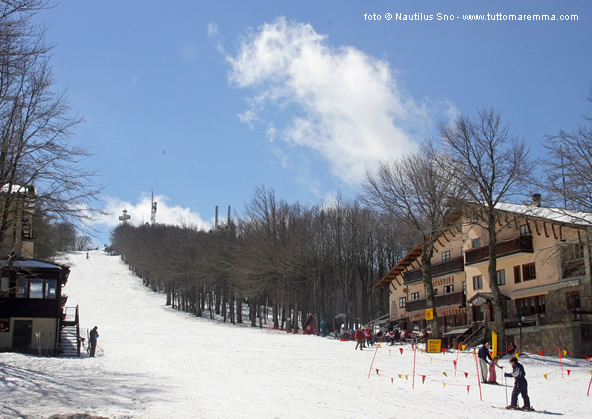 Winter sports scene at Monte Amiata, Siena with view of a ski resort, ski lift, and a skier gliding down. A quaint chalet rests nearby, painted beautifully with snowfall.