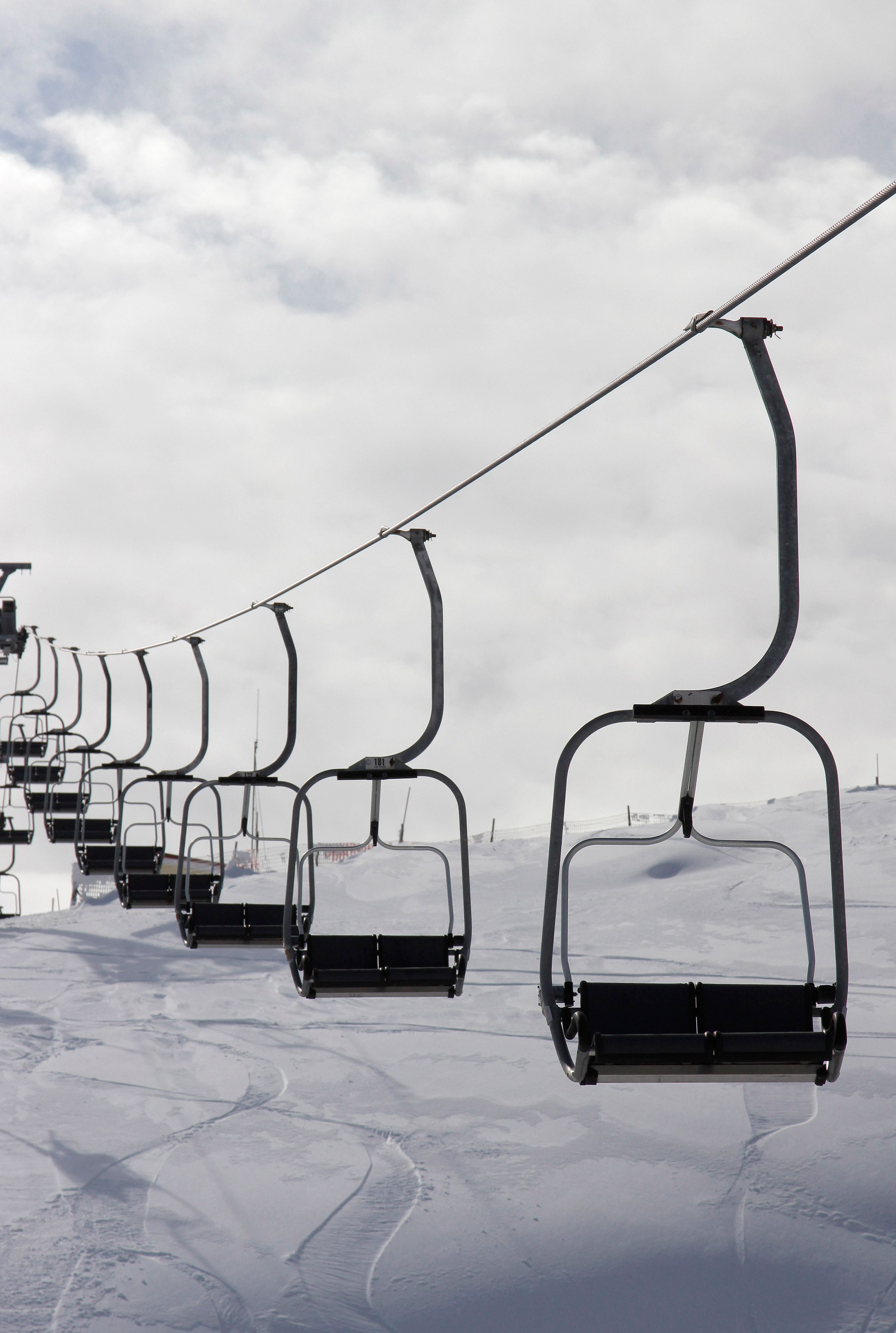 Ski lift ascending a snowy mountain in Seli, Kato Vermio, Greece. Included is a faint image of a bustling ski resort and winter sports enthusiasts enjoying their day in the snow.
