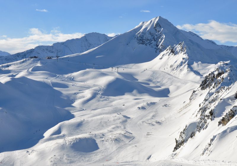 A skier gliding down the slope at Les Arcs | Peisey-Vallandry ski resort in Auvergne-Rhône-Alpes, France. The stunning mountain range and a challet complete the winter sports scene.