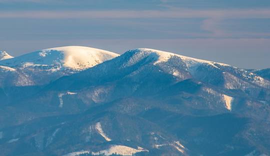Scenic view of Martinské Hole in Slovakia, highlighting a prominent mountain heavily blanketed with snow. A chalet peeks out in the winter landscape, hinting at nearby winter sports activities.