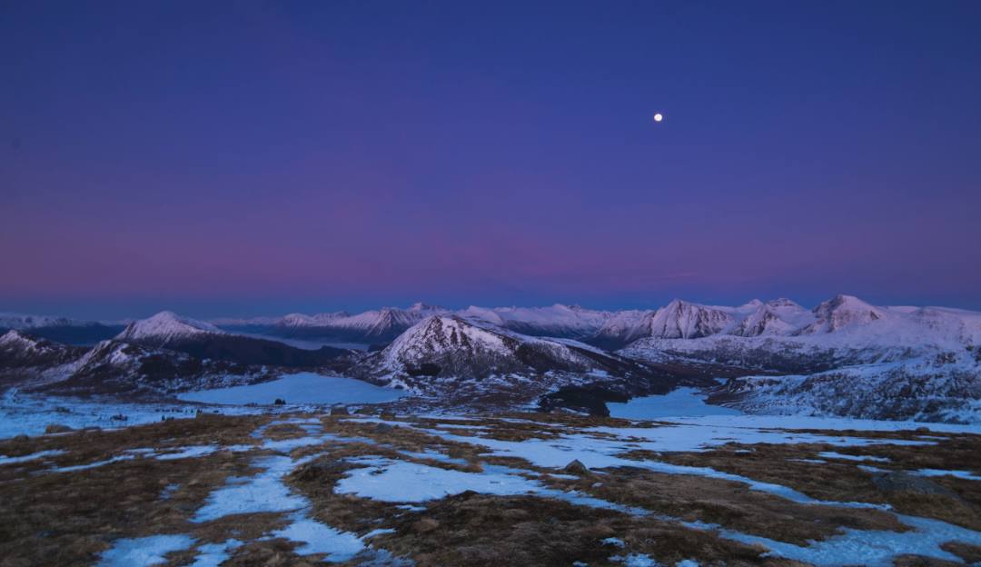 Stunning winter scenery at Sunnmørsalpane Skiarena Fjellsætra in Western Norway featuring a mountain backdrop, a quaint chalet, and signs of winter sports activities.