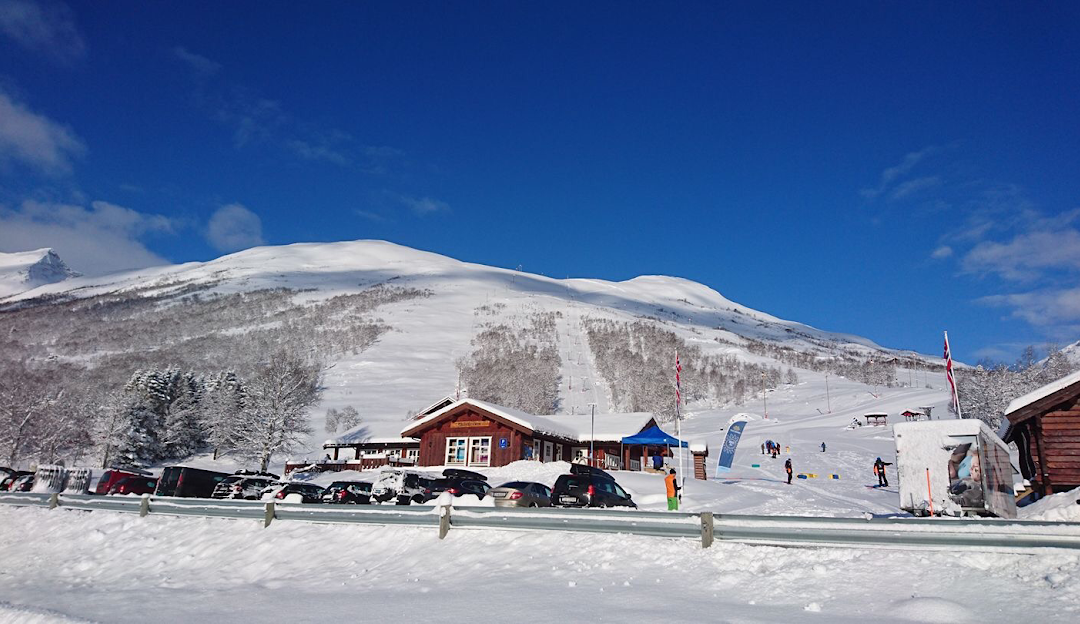 A stunning view of Sunnmørsalpane Skiarena Fjellsætra in Straumgjerde Norway showcasing the ski slopes winter sports enthusiasts active among snow laden landscape and a cozy chalet.
