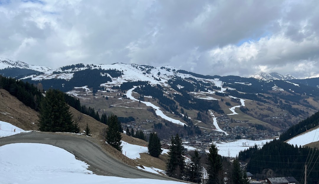 A chalet and ski resort in the Tyrol region of Austria, with snow-covered slopes and mountains. The scene depicts winter sports activities at Reitherkogelbahn.
