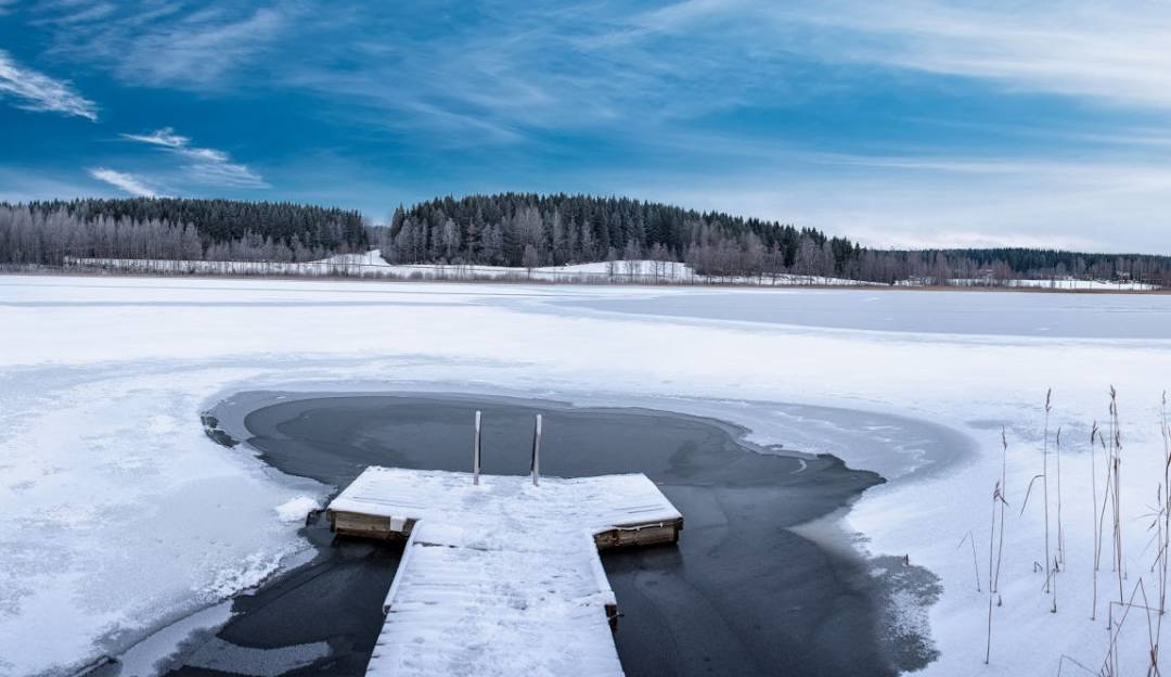 A picturesque winter scene in Himos Jämsä Finland featuring snow-covered slopes bustling with winter sports activities a tranquil icy lake nearby and a cozy chalet nestled in the distance.