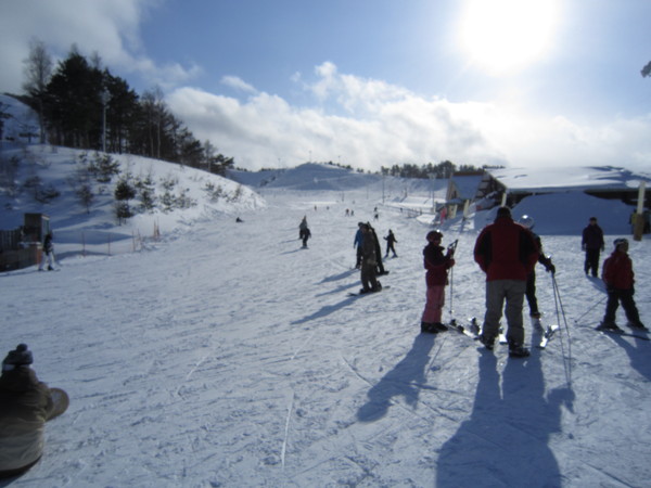 Winter sports scene at Moya Hills in Tōhoku, Aomori, Japan, featuring a ski resort with a chalet, and a family enjoying skiing activities.