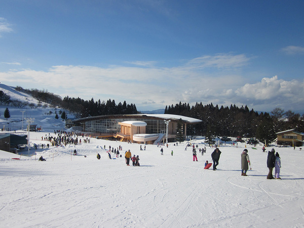 Winter sports scene at Moya Hills in Tōhoku, Japan featuring ski enthusiasts enjoying the slopes near a ski resort and chalet in a snowy landscape.