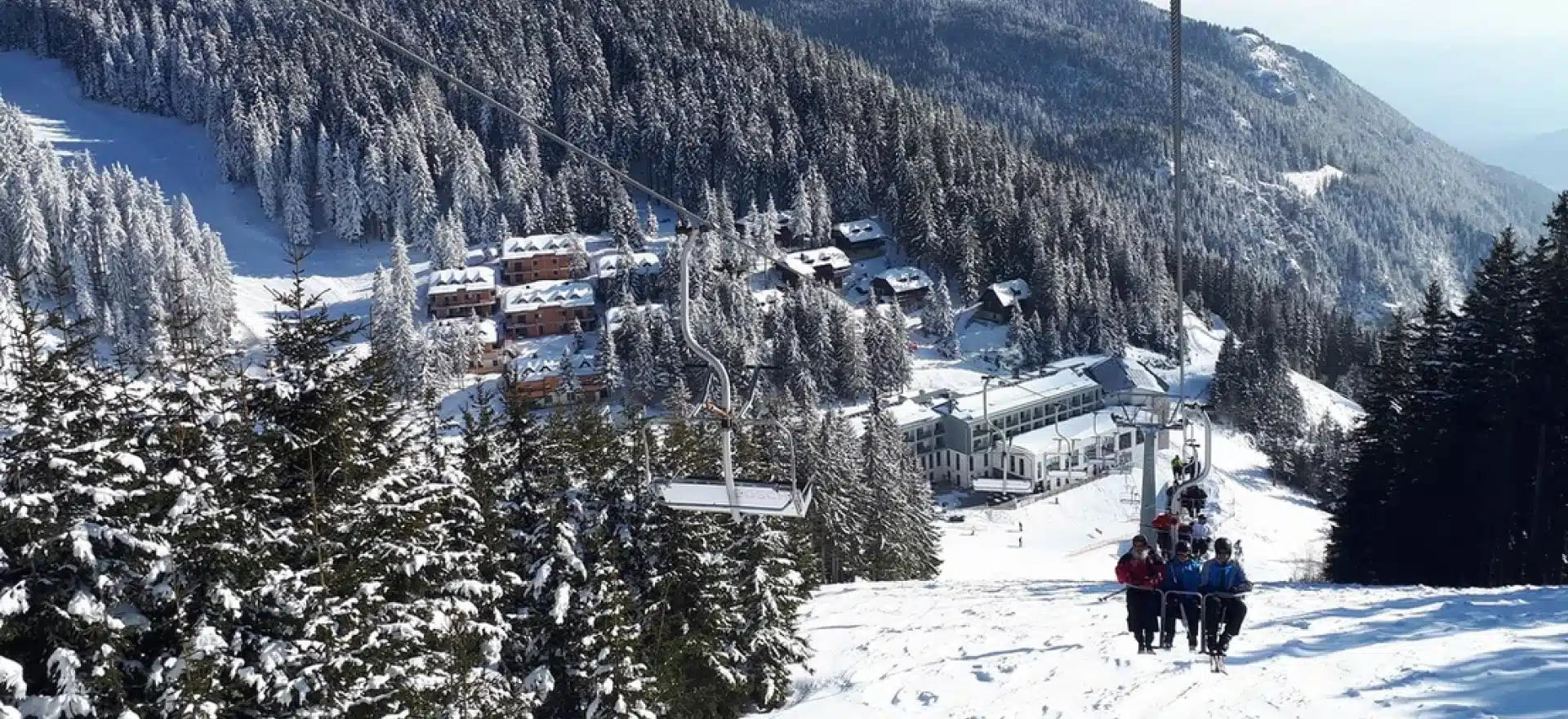 A bustling ski resort scene at Golte in Slovenia featuring a welcoming chalet various winter sports activities underway and a skier gliding down the slopes.