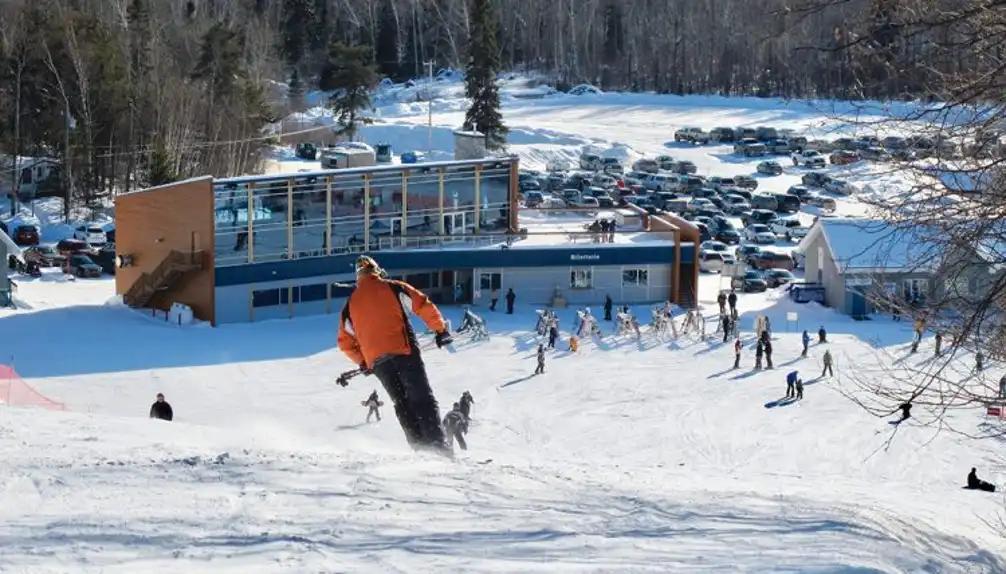 Winter sports scene captured at Mont-Kanasuta, Quebec. Skier glides down the slope amidst the snow-covered landscape, with ski lifts and resort buildings visible in the background.