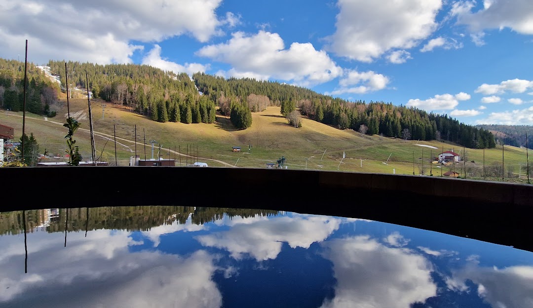 Image showing a picturesque ski resort in La Serra France with a ski lift in view. The scenic winter sports scene is enhanced by a nearby lake and a charming challet. The tranquil snow-covered landscape embodies the charm of Bourgogne-Franche-Comté.