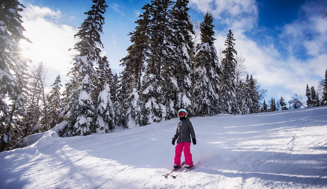 A skier enjoying a winter's day at Mont-Vidéo Ski Resort in Barraute, Quebec. Snowboarders can be spotted in the distance, and a charming chalet peeks through the snowy landscape.