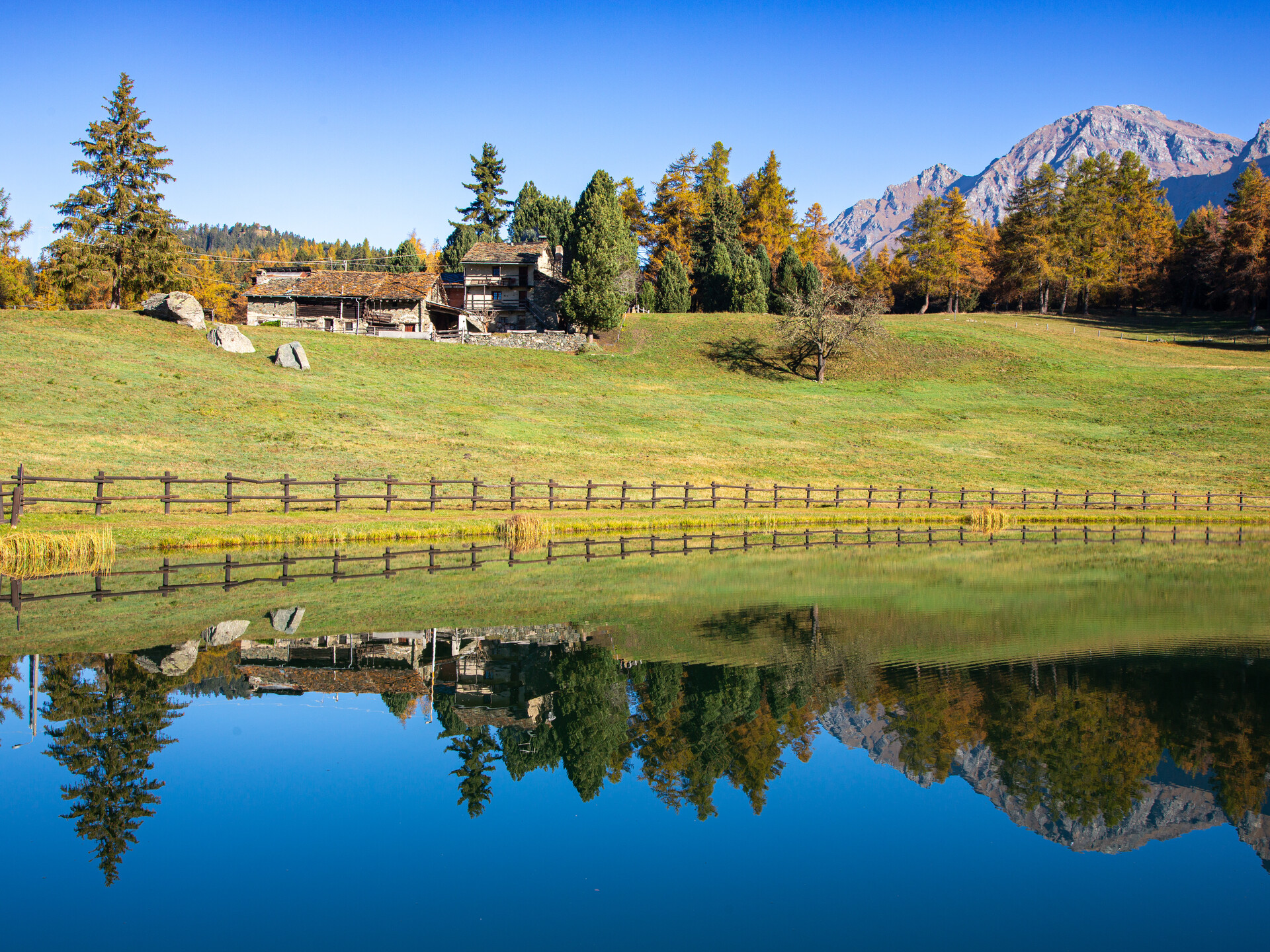 Overview of Colle di Joux ski resort in Italy. The image showcases a bustling winter sports centre, a ski lift ascending the snow-covered mountain, a cozy chalet, and a serene lake nestled in the scenic landscape.