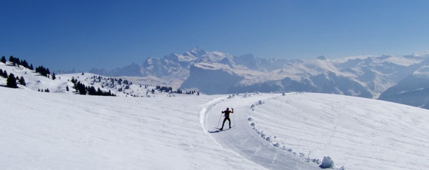 Skiier gliding down the snowy slopes of Colle di Joux in Italy's Aosta Valley, with a quaint chalet and the vibrant ski resort in the backdrop.