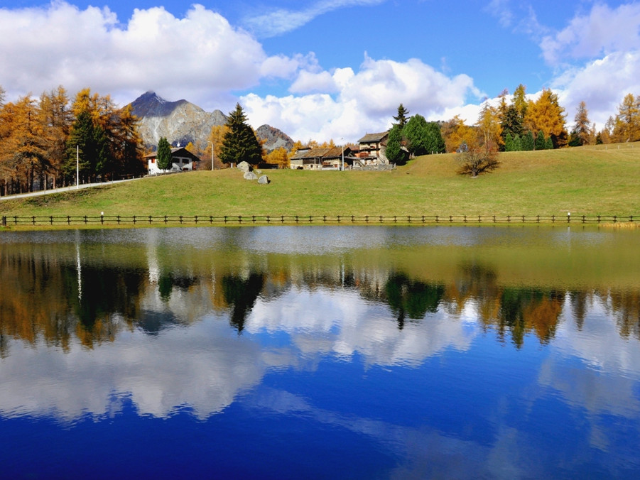 View of Colle di Joux and Mont Avic in Italy featuring a tranquil lake adjacent to a ski resort including a charming chalet symbolizing a serene winter sports destination.