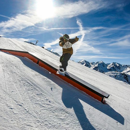 A skier and snowboarder navigating the snowy slopes at Hochzeiger – Jerzens ski resort in Tyrol, Austria, with a chalet nestled in the background.