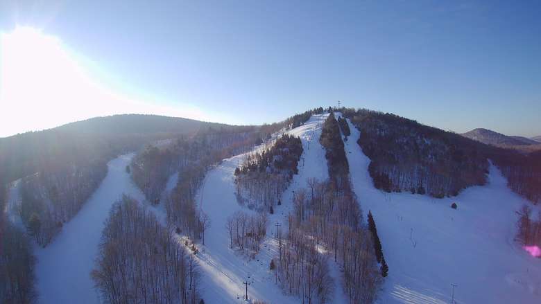 McCauley Mountain Ski Center in USA - the sun is shining over a snowy mountain.
