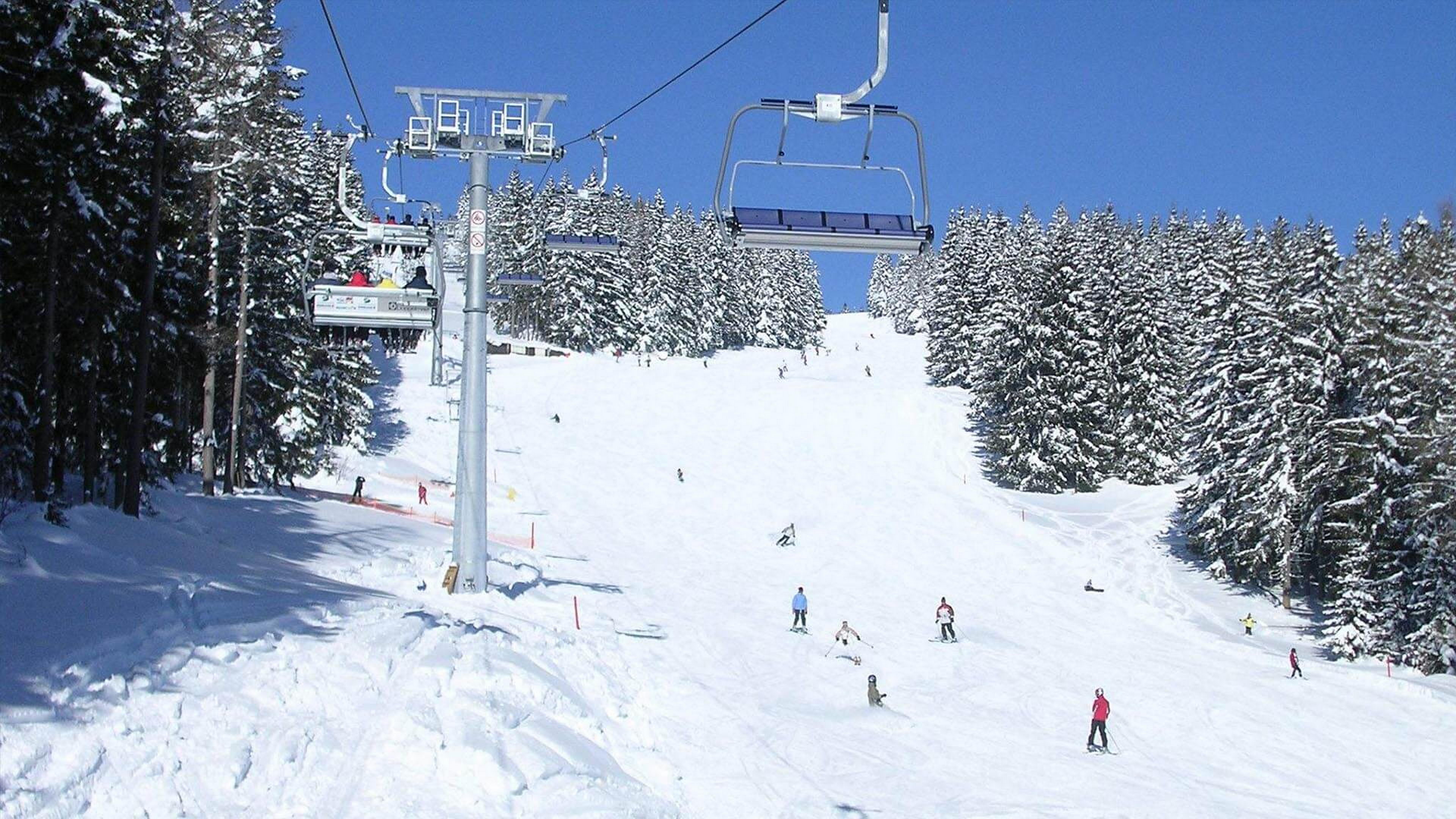 A winter scene at Ski-Waldheimat Hauereck in Austria featuring a bustling ski resort with a ski lift ascending up the mountainside a charming chalet and a skier enjoying the slopes.