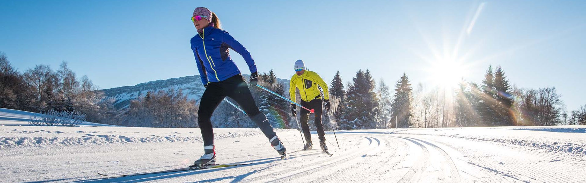 Winter sports scene at Savoie Grand Revard featuring a skier swiftly descending a snow-covered slope, with a bustling winter sports centre and rustic chalet nearby.