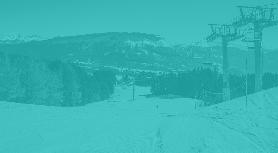 View of the bustling Savoie Grand Revard ski resort in France featuring a ski lift ascending the snow-covered mountain a skier carving through the terrain and a lively winter sports scene.