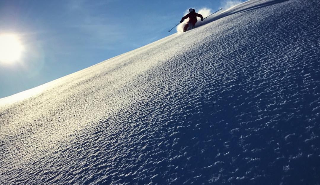 A skier navigating a snowy terrain amidst the vast, wintry landscape of Hallingskarvet in Hovet, Norway. A chalet nestles in the backdrop of this winter sports scene.