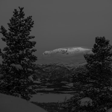 View of the majestic Hallingskarvet mountain in Hovet, Buskerud, Norway, blanketed by a layer of snow. The winter scene also features a solitary chalet amidst the breathtaking snowy terrain.